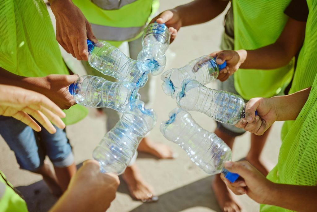Hands group, circle and plastic bottles in beach waste management, community service and climate ch